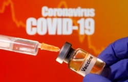 FILE PHOTO: A small bottle labeled with a "Vaccine" sticker is held near a medical syringe in front of displayed "Coronavirus COVID-19" words in this illustration taken April 10, 2020.