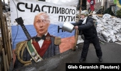 UKRAINE – A pro-European integration supporter washes a banner with an image of Russian President Vladimir Putin near a barricade in Independence Square where the supporters are holding a rally, in Kyiv January 9, 2014