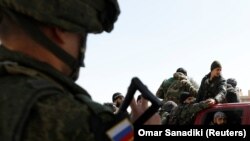 SYRIA -- A Russian soldier gestures to Syrian soldiers at a checkpoint near Wafideen camp in Damascus, Syria March 2, 2018