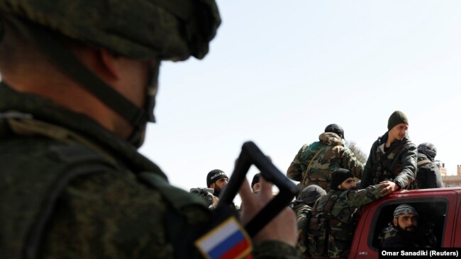 SYRIA -- A Russian soldier gestures to Syrian soldiers at a checkpoint near Wafideen camp in Damascus, Syria March 2, 2018