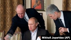 Businessman Yevgeny Prigozhin, left, serves food to Russian Prime Minister Vladimir Putin, center, during dinner at Prigozhin's restaurant outside Moscow, November 11, 2011. (Mikhail Japaridze/AP))