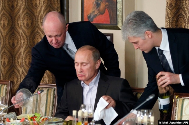 RUSSIA -- Businessman Yevgeny Prigozhin, left, serves food to Russian Prime Minister Vladimir Putin, center, during dinner at Prigozhin's restaurant outside Moscow, November 11, 2011