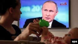 Russia -- A Russian woman plays with her baby while watching the televised call-in show with President V;adimir Putin. in Moscow, April 14, 2016.