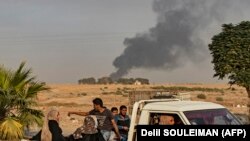 Syrians ride a pickup truck past smoke as Arab and Kurdish civilians flee following Turkish bombardment on Syria's northeastern town of Ras al-Ain in the Hasakeh province along the Turkish border on October 9, 2019.