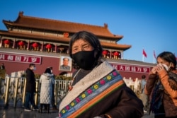 Tourists from Tibet wearing a protective mask (R) and a scarf as a mask (C) walk in front of the portrait of late communist leader Mao Zedong (back) at Tiananmen Gate in Beijing on January 23, 2020.
