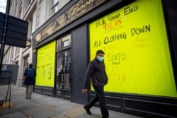 A man wearing a protective face covering to combat the coronavirus walks past sales boards in the windows of a shop in London on November 10, 2020.