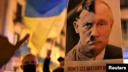 A person holds a banner with the joined faces of a portrait of Vladimir Putin and Adolf Hitler during an anti-war protest in Barcelona, Spain, February 24, 2022. REUTERS/Nacho Doce