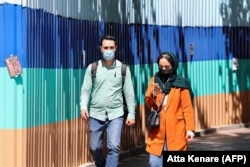Iranians wearing protective masks walk on a sidewalk in the capital Tehran, April 12, 2021.