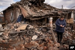 A woman holds a piece of shrapnel standing in the rubble of a house where Ukrainian servicemen were sheltering in Kupiansk on February 20, 2023. The house was destroyed by a Russian rocket strike. (Vadim Ghirda/AP)
