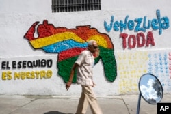 A man walks in front of a mural of the Venezuelan map showing the Guyana administered and controlled Essequibo territory included, in Caracas, Venezuela, on November 29, 2023. (Matias Delacroix/AP)