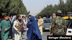 Taliban forces block the roads around the airport, while a woman with Burqa walks passes by in Kabul, on August 27, 2021. (Reuters)
